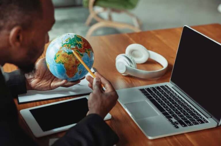 Person studying globe at desk with laptop