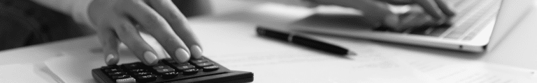 Hand using calculator beside laptop and paperwork